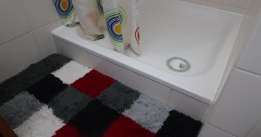 Duşa girip çıkan kadın bacakları, duş perdesini kapatan kadın, ferahlatıcı bir duş alacak, kırmızı, mavi ve beyaz renkli minder. Evde hijyen ve rahatlama kavramı