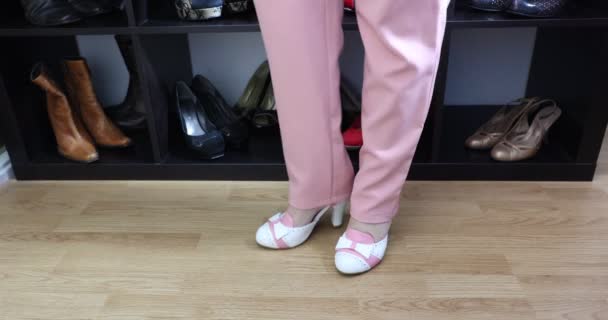 穿着粉色裤子的腿和站着的成年女子的女性脚 穿着白色 粉色高跟鞋和蝴蝶结 家里更衣室里有鞋柜 魅力和时尚观念 — 图库视频影像