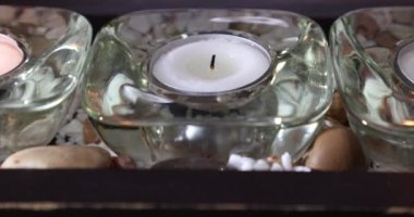Cam mum tutacağında bir kibritle bir çay mumu yakarken, diğer iki mum, küçük taşlar arasında, sükunet ve huzur hissi veren, sarı alev. İnanç ve umut kavramı