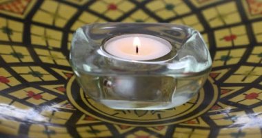 Sarı bir plaka üzerinde cam mum tutacağında çay farı, esintiyle sönen ya da bulanık bir arka planda siyah kare dekorla söndürülen. İnanç ve umut kavramı