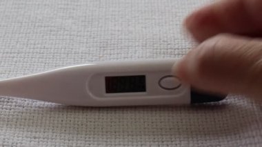 Yetişkin kadın ellerinin dijital vücut termometresini alıp açması 33 ile 34.2 arasında değişen 36.5 derece sıcaklığa işaret ediyor.