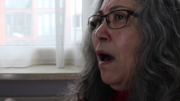 インフルエンザのくしゃみをする高齢の成人女性 ハンカチで鼻と口をカバー ぼやけた背景ウィンドウ コロナウイルスによる自宅監禁 メガネ 波状灰色の髪 呼吸器疾患の概念 — ストック動画