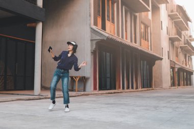 Müzik dinleyen ve kulaklıkla sokakta akıllı telefonlardan eğlenen mutlu Asyalı genç kadın..