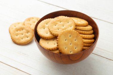 Tahta bir kraker kasesinde yuvarlak kraker, beyaz tahta masa arka planında..