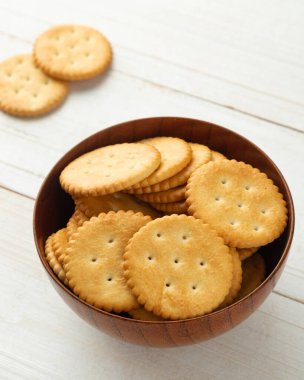 Tahta bir kraker kasesinde yuvarlak kraker, beyaz tahta masa arka planında..