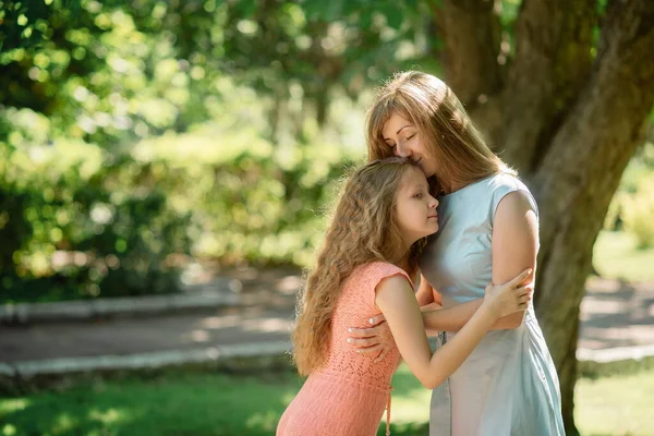 Genç bir anne ve kız parkta yürürken sarılıyorlar. Tek ebeveyni ve çocuğu olan güzel bir ailenin portresi.
