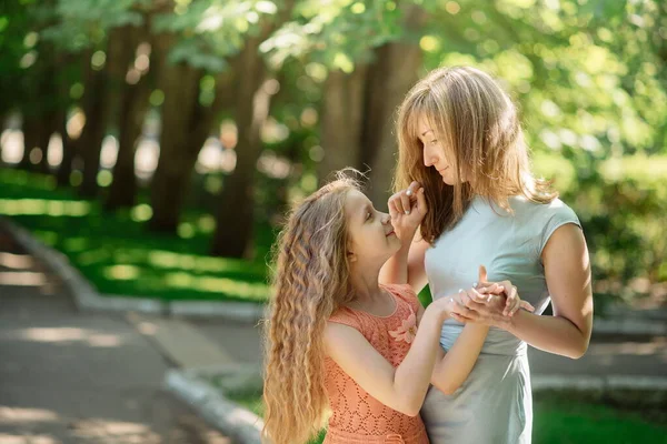 Genç bir anne ve kız parkta yürürken sarılıyorlar. Tek ebeveyni ve çocuğu olan güzel bir ailenin portresi.