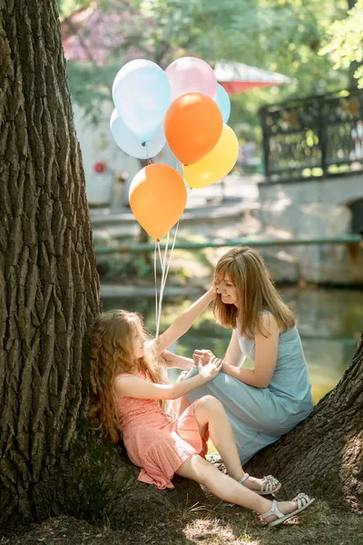 Şirin bir aile annesi ve kızı yaz parkında doğum günü kutlaması için balon fırlatıyorlar.