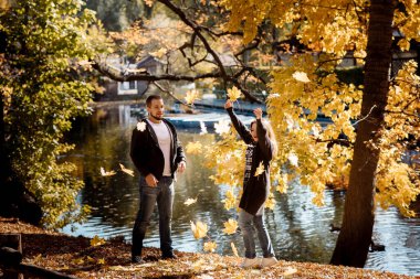 Genç erkekler ve kadınlar sonbaharda yapraklar dökülürken sonbahar yapraklarını parka kusarlar.