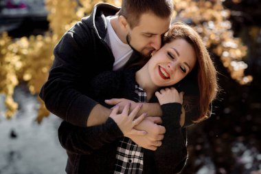 Güz mevsiminde yaprakların arasında, parkta sarılan genç bir çift.