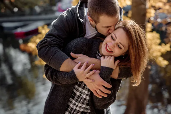 秋には池の近くの公園で抱き合っている美しい若い夫婦と女性 — ストック写真