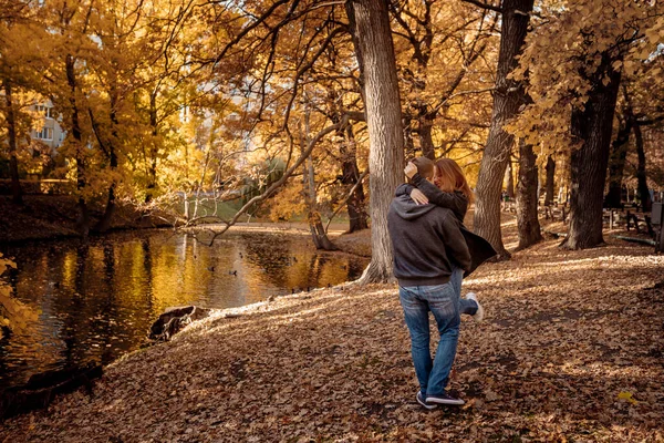 秋叶落叶时 一个残忍的年轻人抱着心爱的女人在池塘边散步 图库图片