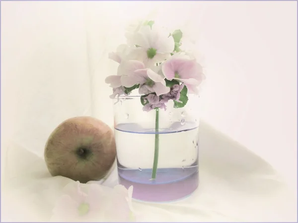 A bunch of white flowers in a glass with water and a manzana — Stock Photo, Image
