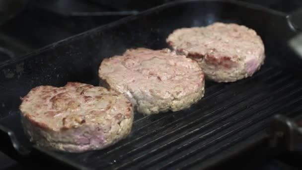 Las hamburguesas de carne se ponen con espátula en una parrilla de sartén con recubrimiento antiadherente en aceite de oliva salpicado. El proceso de cocción en la cocina. — Vídeos de Stock