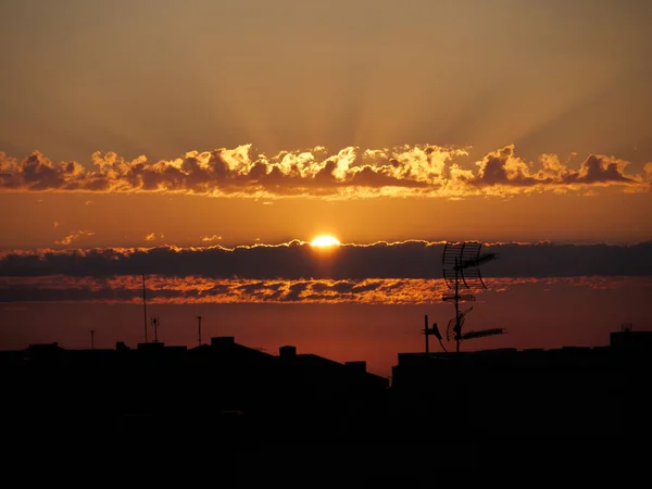 Драматическое небо восхода солнца над крышами города. Городской пейзаж с солнцем, сияющим сквозь облака. — стоковое фото