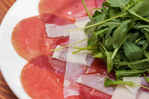 Red beef carpaccio in a white plate with arugula and parmesan cheese. — Stock Photo, Image