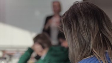 Konferans salonunda arka planda bir kadının, arka planda beyaz tahtayla ders veren bir profesörü dinlemesi..