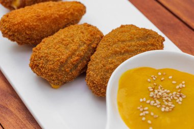 Beyaz tabakta sarı soslu kızarmış kroket. Ahşap arkaplanda yan görünüm.