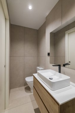 Yenilenmiş dairede modern tarz banyo. Lavabosu, siyah musluğu ve aynası olan dar tuvalet.