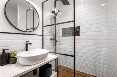 Siyah duşlu, yuvarlak aynalı ve klasik beyaz fayanslı basit bir banyo.