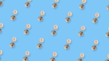 Mavi arka planda izole edilmiş renkli donut deseni. Donutla kusursuz desen. Çörekler. Üst Manzara. Gerçekçi animasyon. 4K video hareketi