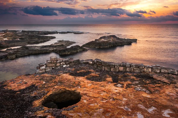 Pôr do sol sobre o mar e costa rochosa com ruínas antigas — Fotografia de Stock