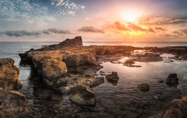 Pôr do sol sobre o mar e costa rochosa com ruínas antigas — Fotografia de Stock