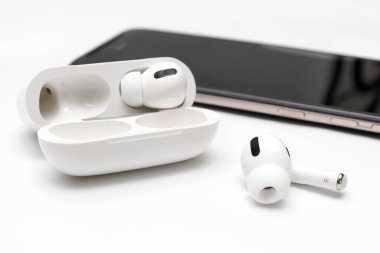 Kablosuz beyaz kulaklık, kablosuz şarj cihazı ve beyaz arka planda akıllı telefon..