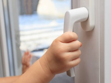 Çocuk pencerenin sapına tutunarak açmaya çalışıyor. Sadece çocukları evde bırakma kavramı, çocukların güvenliği, ebeveynsiz çocuklar....