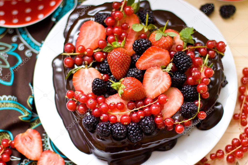 Close up of heart shaped chocolate cake decorated with chocolate frosting, strawberries, blackberries and red currant