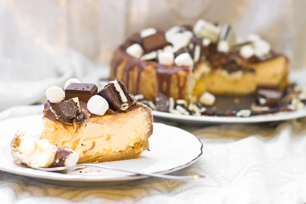 Slice of cheesecake with chocolate ganashe, decorated with mini marshamallows, cookies and chocolate — Stock Photo, Image