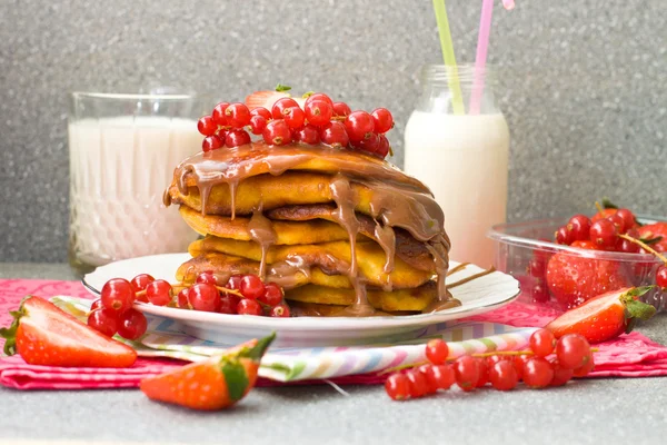 Pannenkoeken met karamel saus, rode bessen, aardbeien en glas melk op de grijze achtergrond — Stockfoto