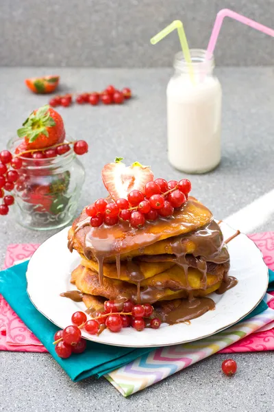 Pannenkoeken met karamel saus, rode bessen, aardbeien en glas melk op de grijze achtergrond — Stockfoto