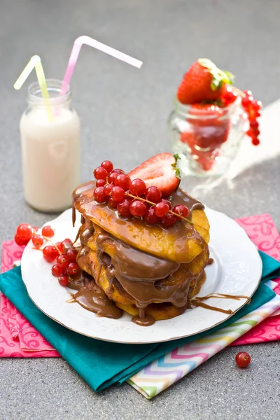 Pannenkoeken met karamel saus, rode bessen, aardbeien en glas melk op de grijze achtergrond — Stockfoto