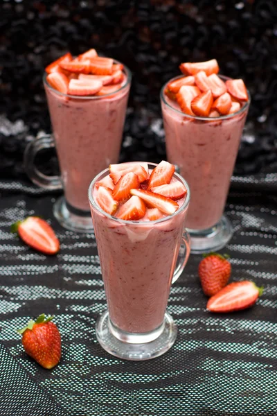 Yoghurt, melk en strawberry smoothie versierd met verse aardbeien op zwarte en zilveren achtergrond, selectieve aandacht op de bovenkant van de glazen — Stockfoto