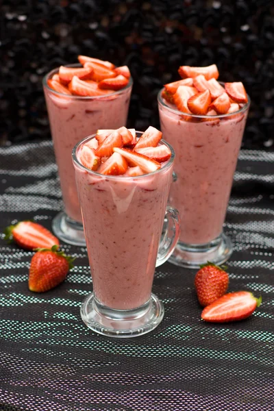Yoghurt, melk en strawberry smoothie versierd met verse aardbeien op zwarte en zilveren achtergrond, selectieve aandacht op de bovenkant van de glazen — Stockfoto