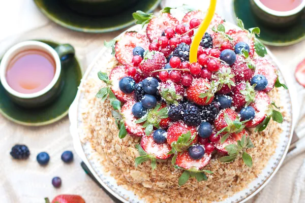 Torta napoleonica, decorata con bacche fresche, fragole, mirtilli e more, con candela di compleanno. Due tazze di tè verde e teiera vicino alla finestra . — Foto Stock