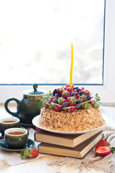 Pastel de Napoleón, decorado con bayas frescas, fresas, arándanos y moras, con vela de cumpleaños. Dos tazas de té verde y tetera cerca de la ventana . —  Fotos de Stock