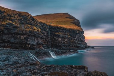 Rocky shore on a cloudy day. Cliffs of Kalsoy island. Early morning in Mikladalur, wild Faroe Islands. November 2021. Long exposure picture clipart