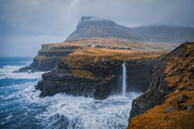 Arka planda Gasadalur köyü ile Mulafossur şelalesinin dramatik manzarası. Vagar Adası, Faroe Adaları, Danimarka. Kasım 2021.