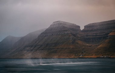 Faroe Adaları, Husar köyü yakınlarındaki Kalsoy adası. Gün batımında pembe gökyüzü ve kayalıkları olan durig alacakaranlığı. Kasım 2021