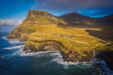 Arka planda Gasadalur köyü ile Mulafossur şelalesinin güneşli manzarası. Vagar Adası, Faroe Adaları, Danimarka. Kasım 2021. Lonf pozlama resmi