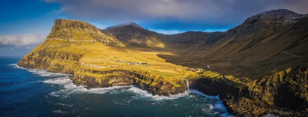 Arka planda Gasadalur köyü ile Mulafossur şelalesinin güneşli manzarası. Vagar Adası, Faroe Adaları, Danimarka. Kasım 2021. Lonf pozlama resmi