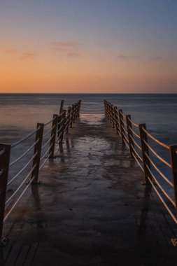 Jetty, güneş doğarken Portekiz Madeira Adası 'ndaki Canico yakınlarındaki çakıl taşlı plajda. Ekim 2021. Uzun pozlama resmi