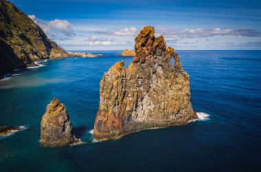 View of the Ilheus da Ribeira da Janela rock islets under a clear blue sky. The rocks form a famous landmark on the northern shore of the island of Madeira, Portugal. Aerial drone shot, october 2021