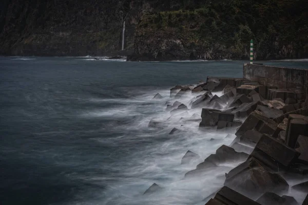 Rock and water lines in a black sand beach with moody cliffs on the background in Seixal at stormy day. October 2021. Madeira, Portugal.