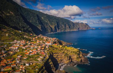Amazing aerial view of red roofed houses located amidst green fields near Seixal beaches washing by ocean in Madeira, Portugal. October 2021