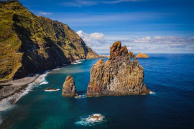 View of the Ilheus da Ribeira da Janela rock islets under a clear blue sky. The rocks form a famous landmark on the northern shore of the island of Madeira, Portugal. Aerial drone shot, october 2021