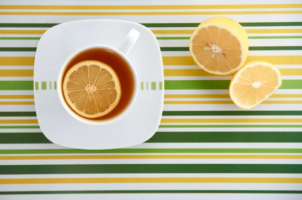 Tasse mit Tee und Zitrone auf bunt gestreiftem Hintergrund — Stockfoto