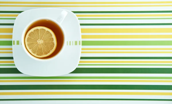 Tasse mit Tee und Zitrone auf bunt gestreiftem Hintergrund — Stockfoto